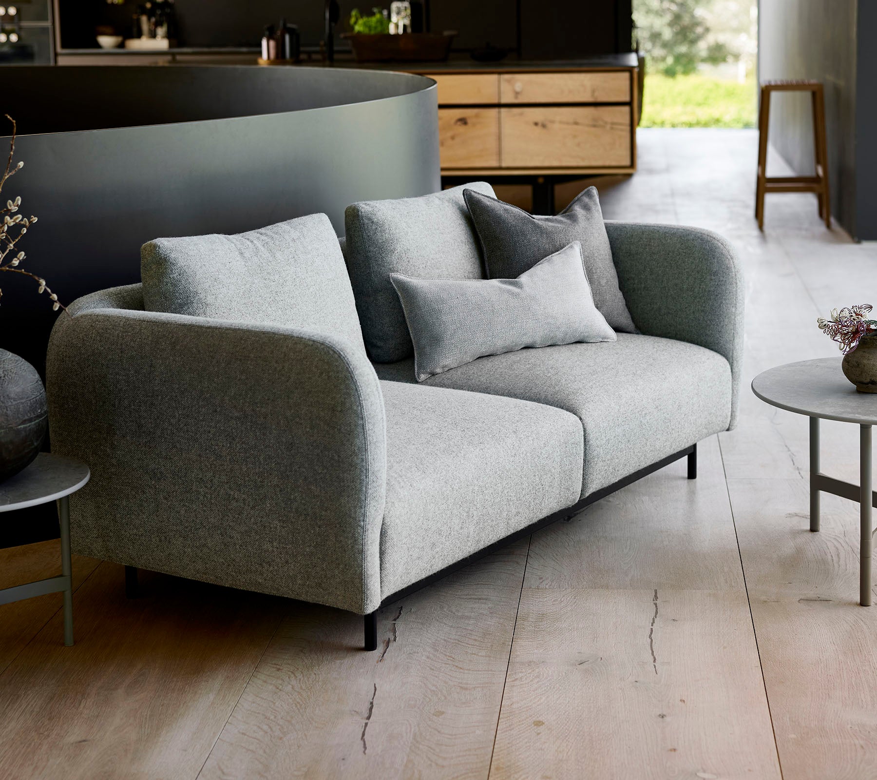 Modern grå soffa med mjuka kuddar, i par med ett litet runt bord, mot en minimalistisk bakgrund.
