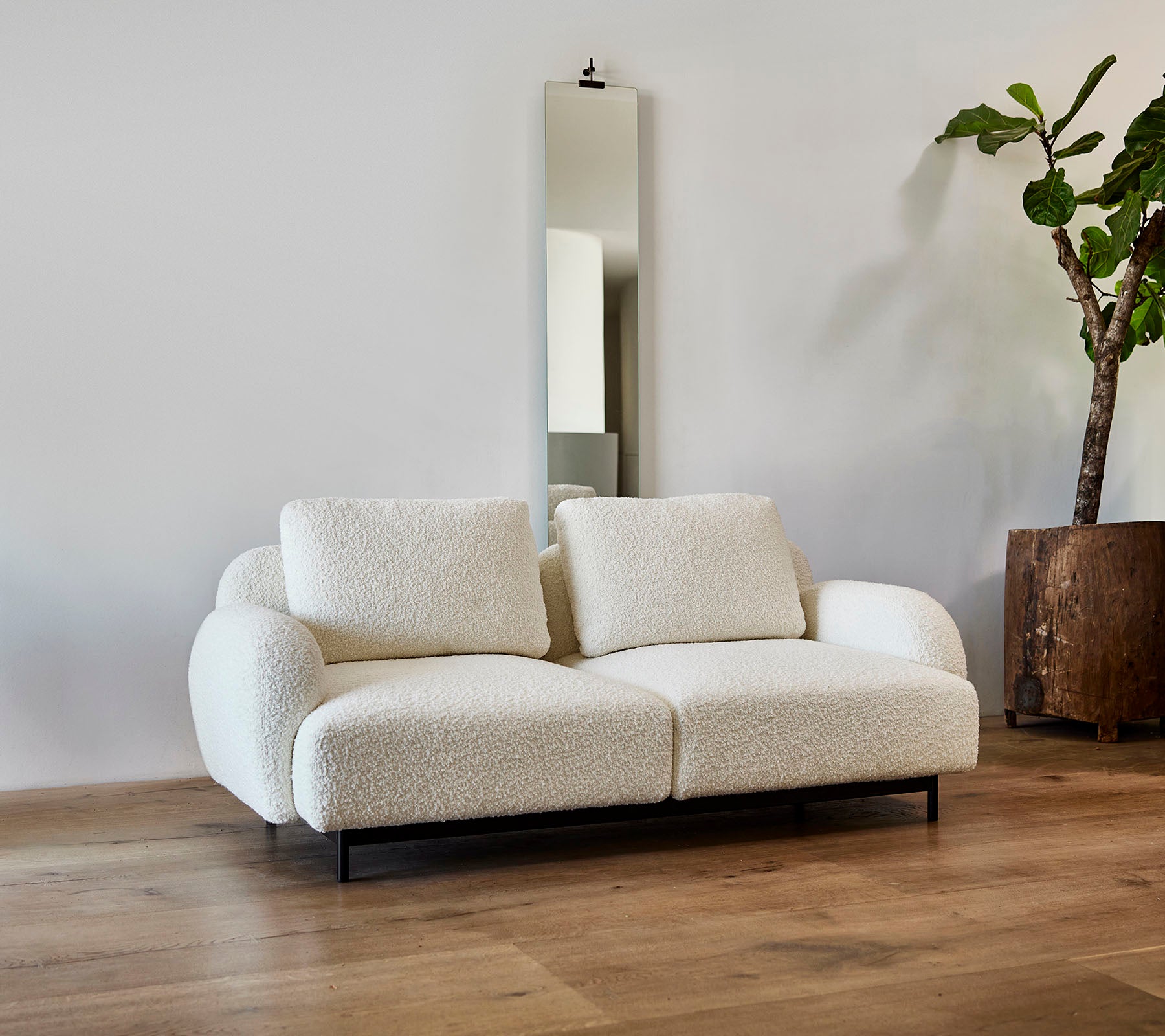 En stilren vit soffa med fluffiga kuddar, tillsammans med en stor spegel och en krukväxt i en modern miljö.