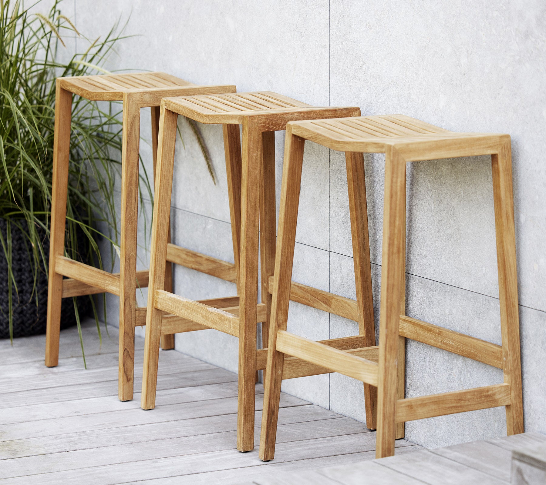 Tre träflipparstolar med spröjsade sitsar, med en minimalistisk design och rena linjer, placerade bredvid en dekorativ växt.