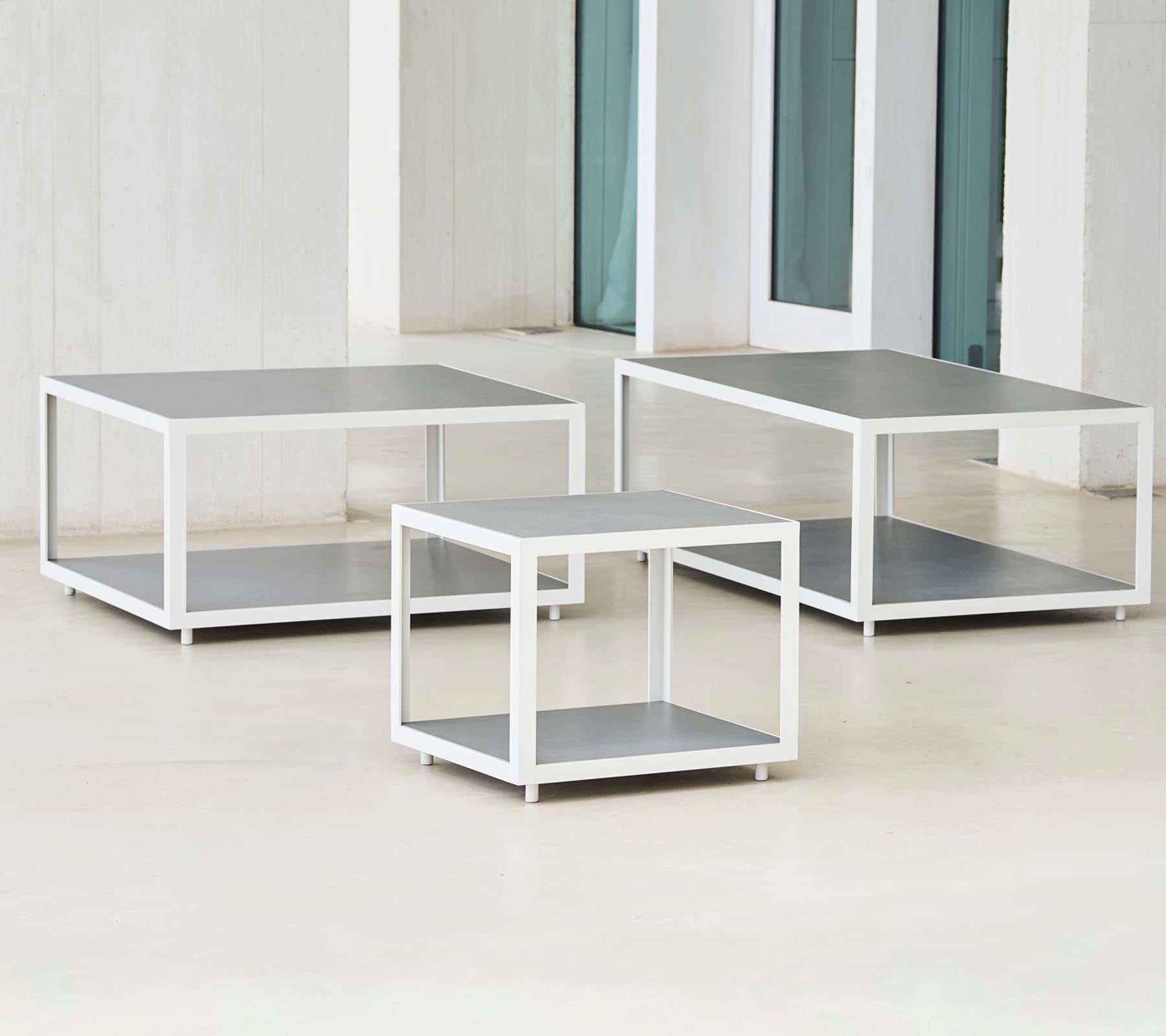 Ett set med tre moderna bord med en stilren design som har metallramar och plana ytor, arrangerade i olika storlekar.