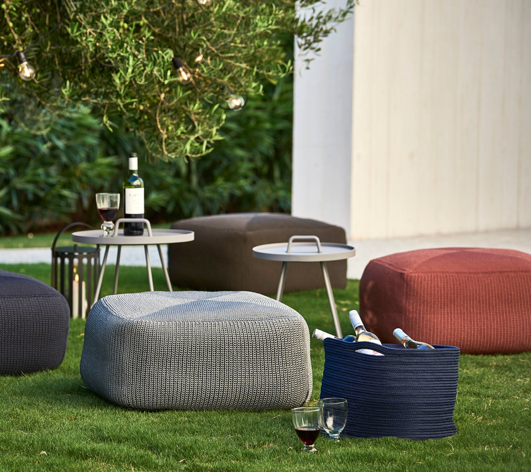 Texturerade poufs i olika färger placerade på gräset, i sällskap av ett litet bord med drycker och vinflaskor.