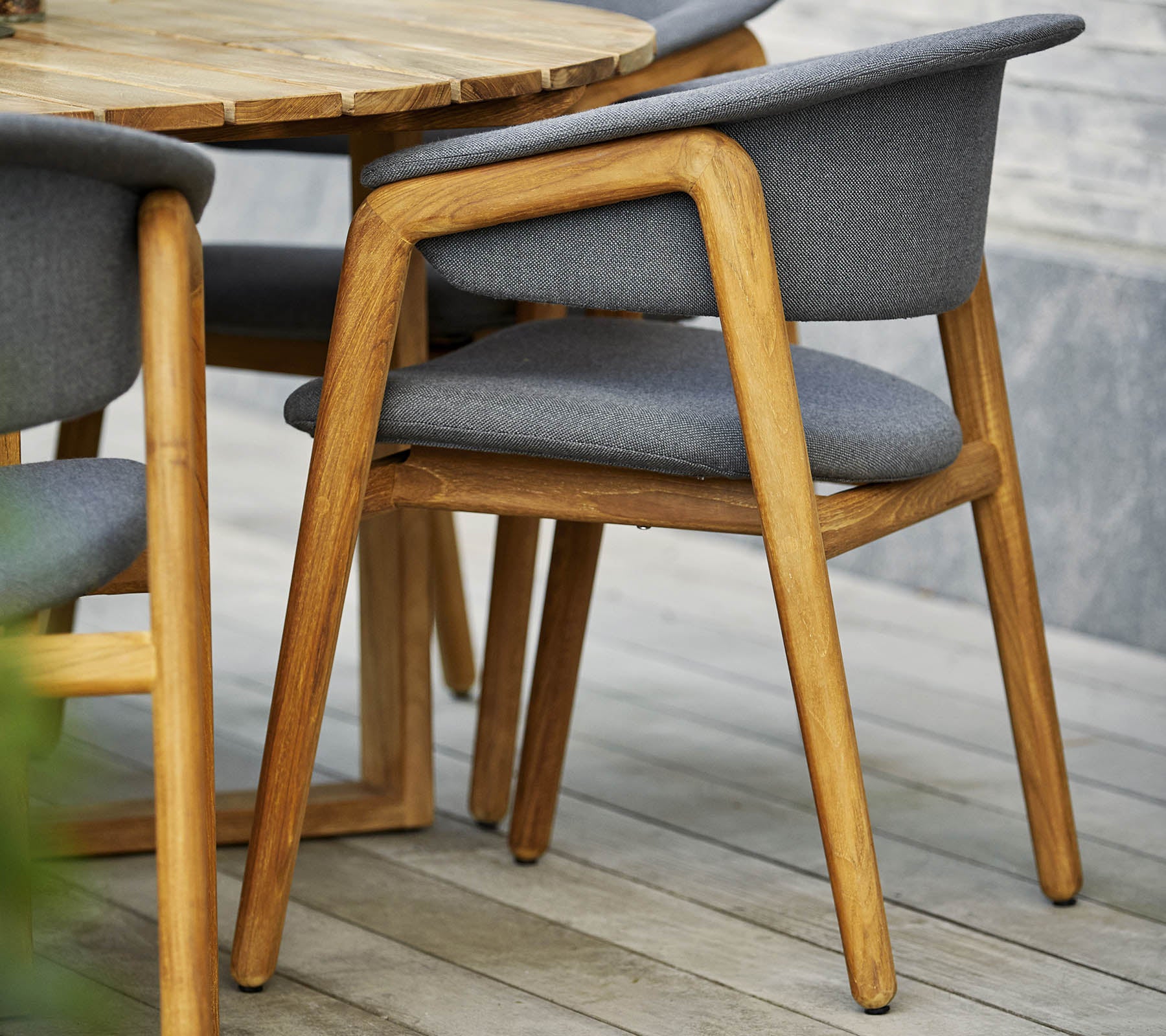 Stilfull trästol med grå klädd sits och ryggstöd, tillsammans med ett runt bord i en modern design.