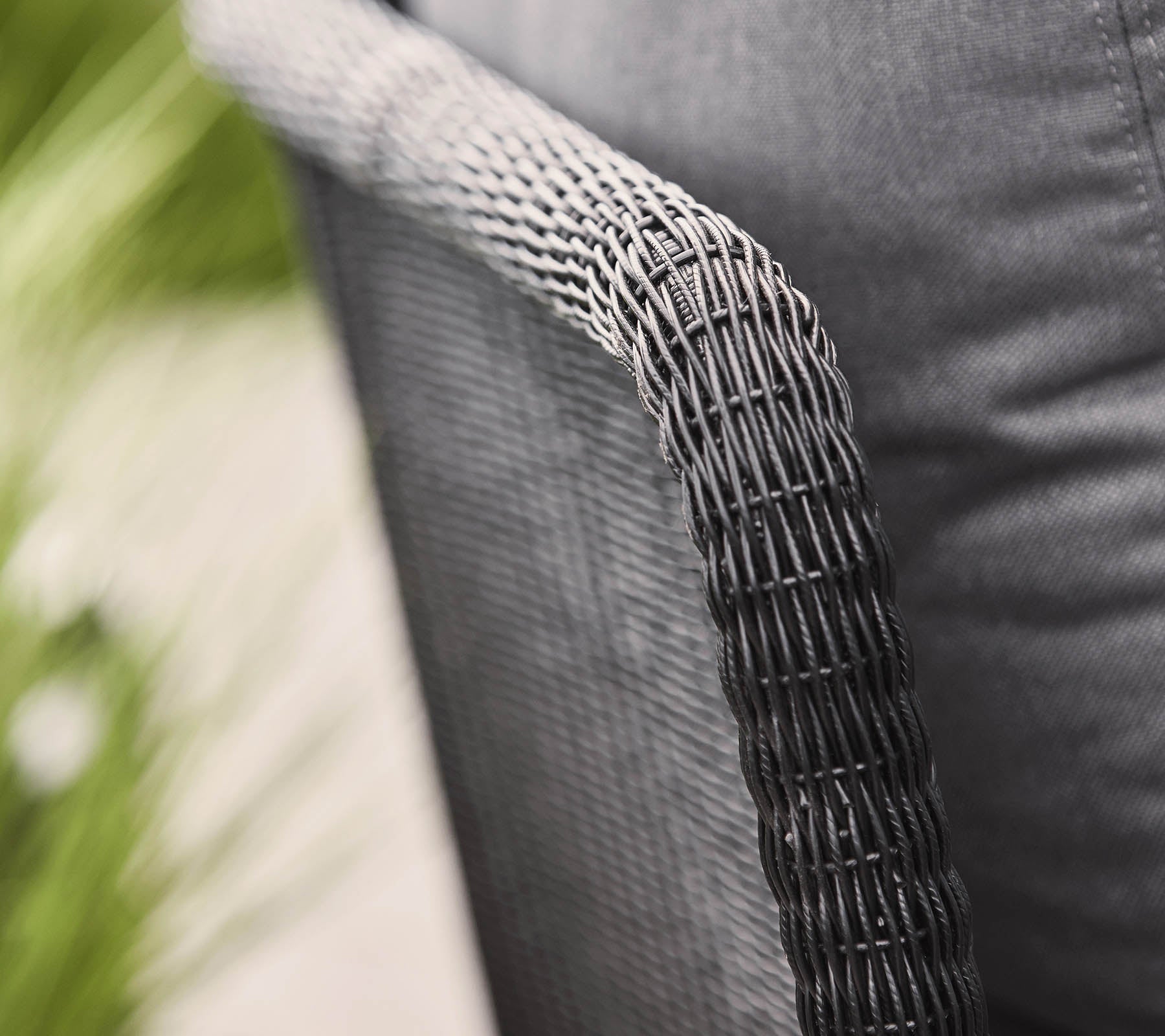 Närbild av ett vävt stolarm med en texturerad svart finish, som visar en modern design och ett mysigt tygsäte.