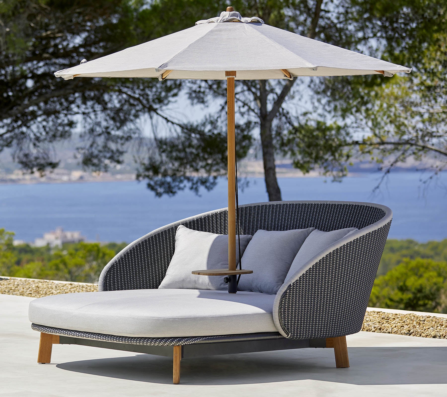 Stilfull utomhus loungesoffa med bekväma kuddar och ett stort parasoll för skugga, placerad mot en naturskön bakgrund.