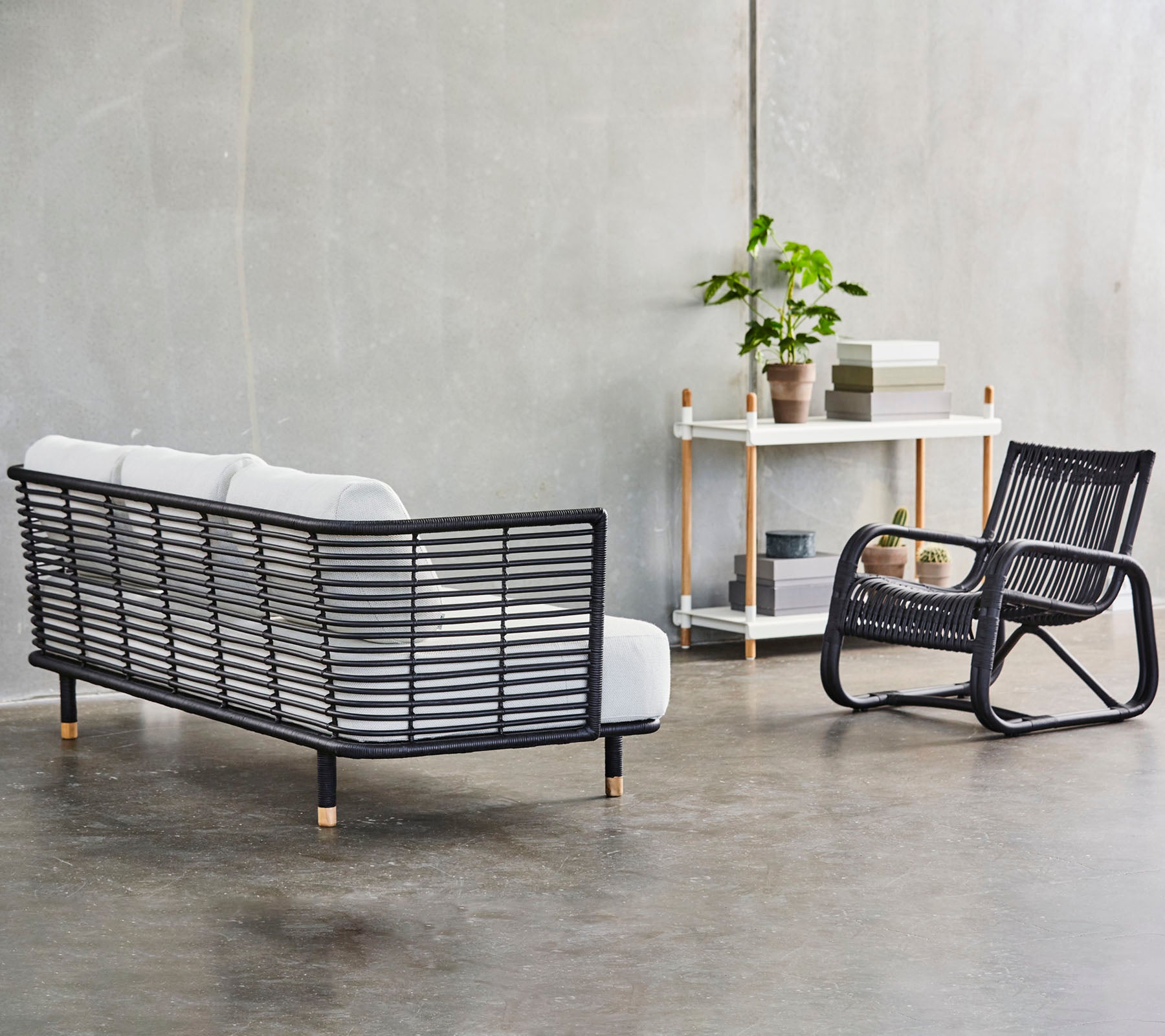 En modern sittarrangemang med en stilren svart ramsoffa med vita kuddar och en matchande gungstol, accentuerad av grönska.