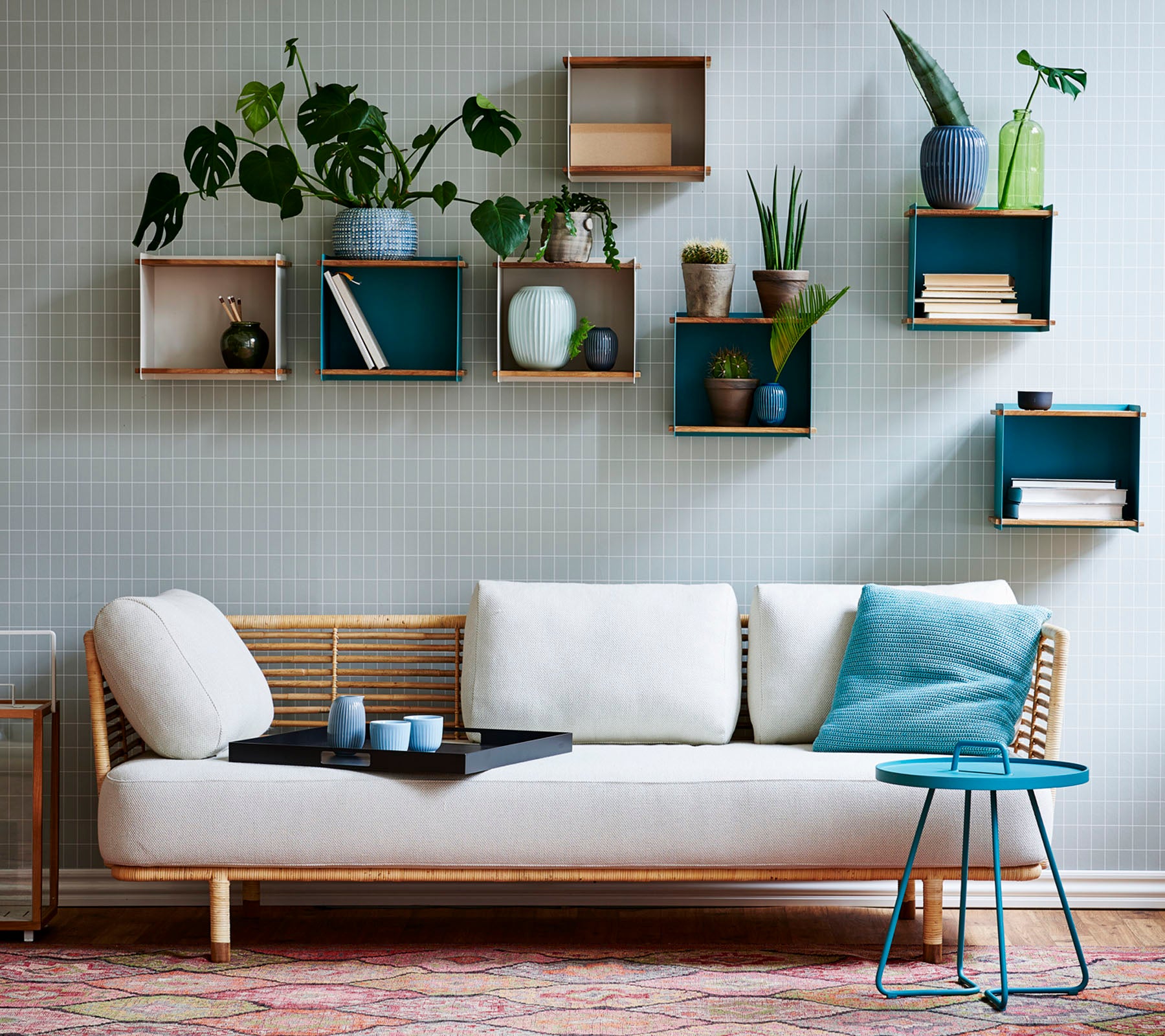 En stilren soffa med ett lätt kuddfodral och ett litet bord, prytt med olika krukväxter som visas på geometriska hyllor.