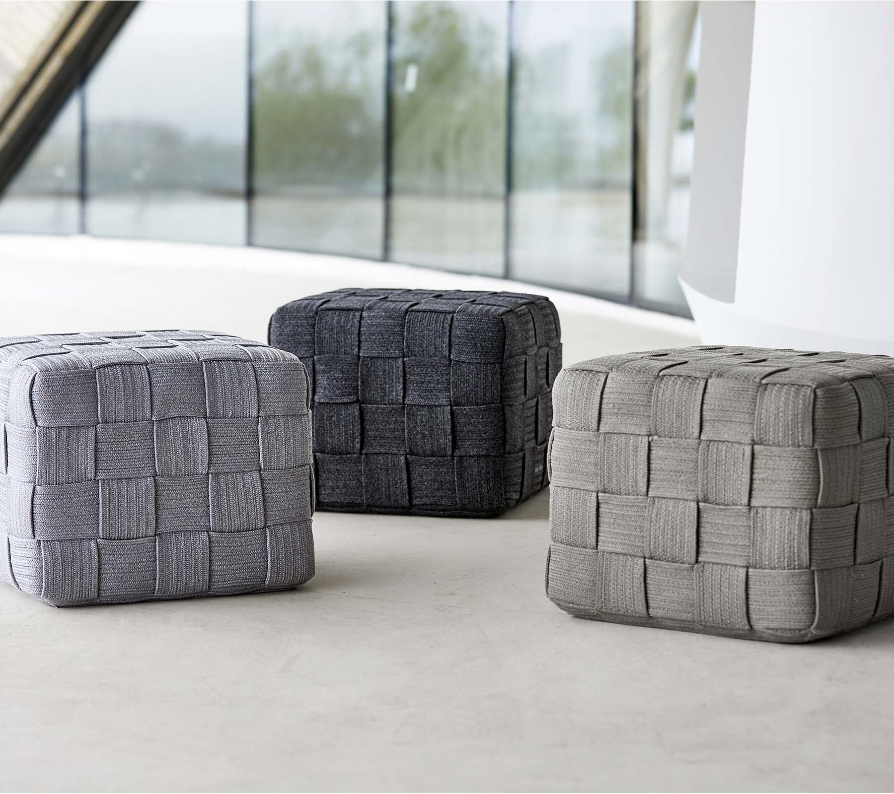 Tre vävda puffar i olika grå nyanser, med en strukturerad design, placerade på en ljus yta. Ideala för sittplatser eller dekoration.