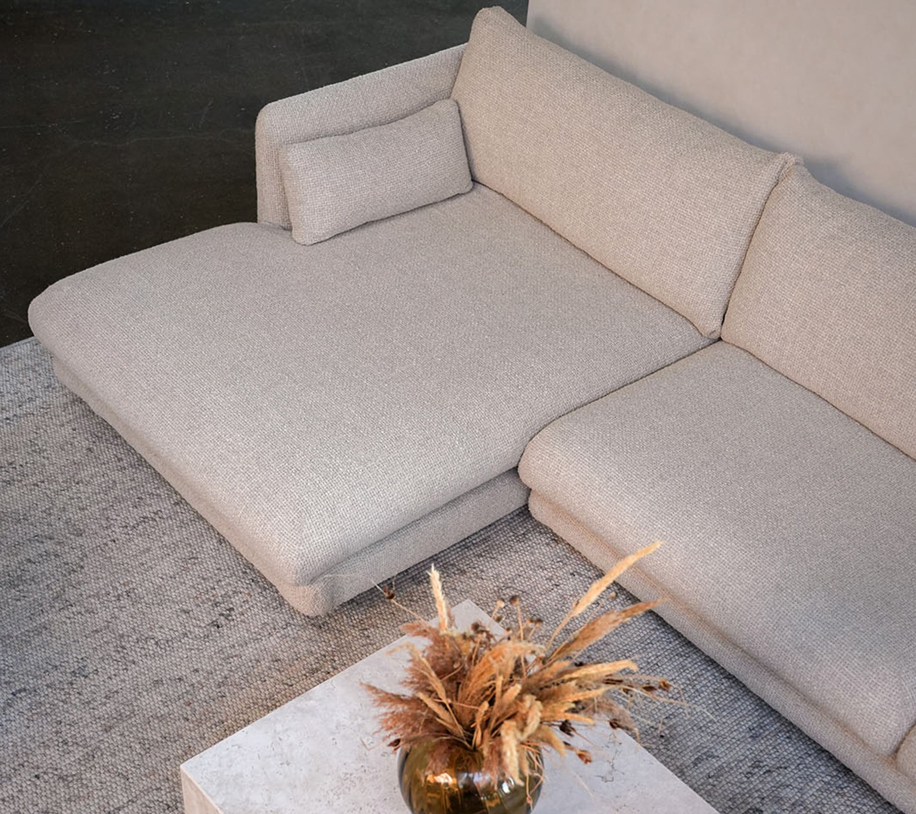 Modern beige soffa med ett vitt bord och en dekorativ vas i en stilren loungeinredning.