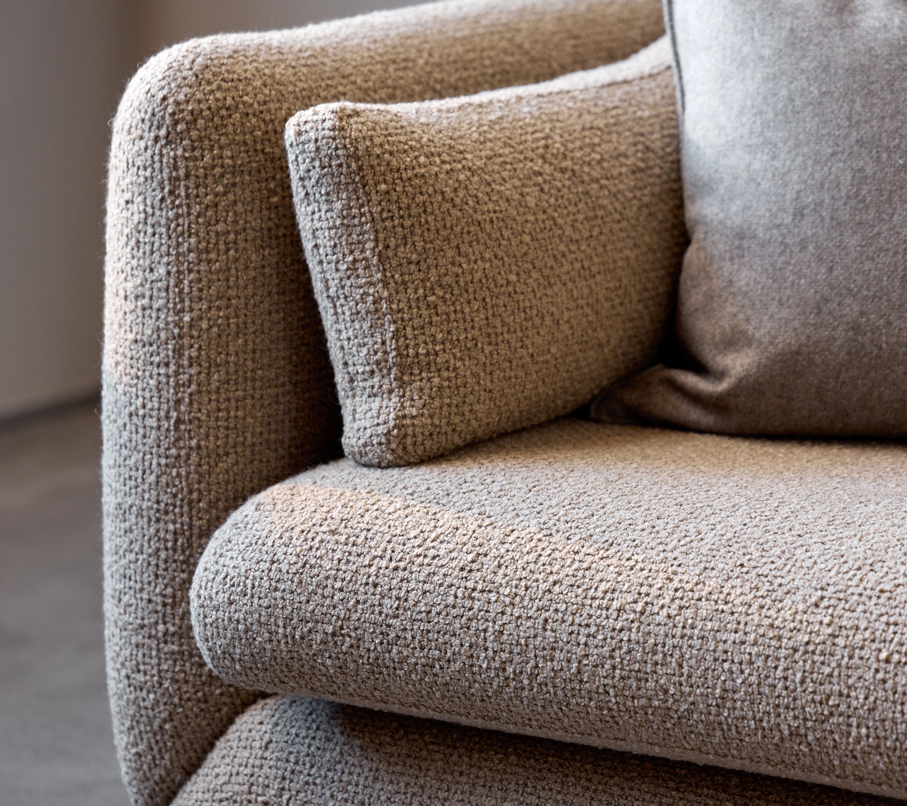 Närbild av en taupe Bloom-soffarmstöd, som visar dess texturerade tyg och mjuka kudde för extra komfort.