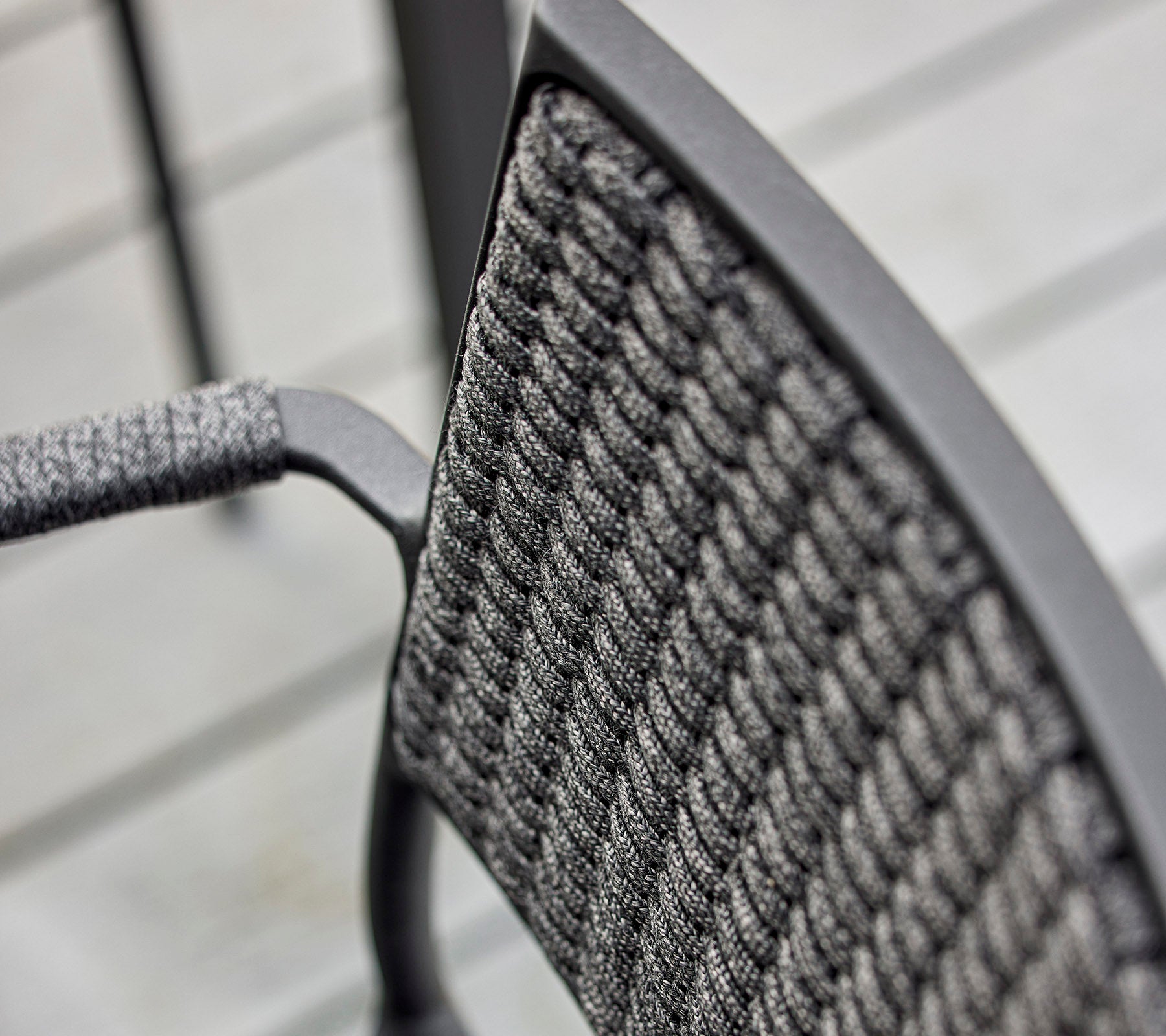 Närbild av en stolrygg med en strukturerad vävd design och en elegant metallram, som betonar modern hantverk.