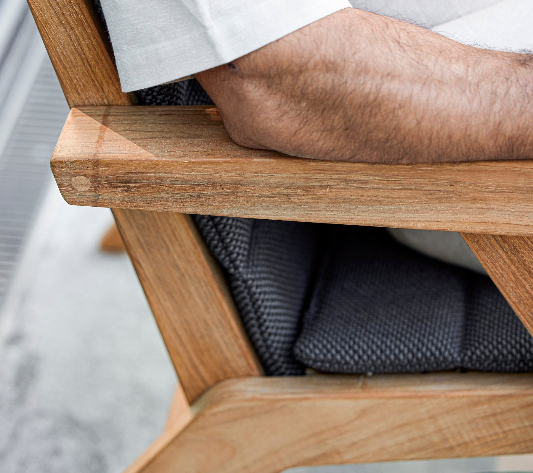 En närbild av en trästolarm med en stoppad sits, som har en arm som vilar på den, och visar en blandning av naturliga och texturerade material.