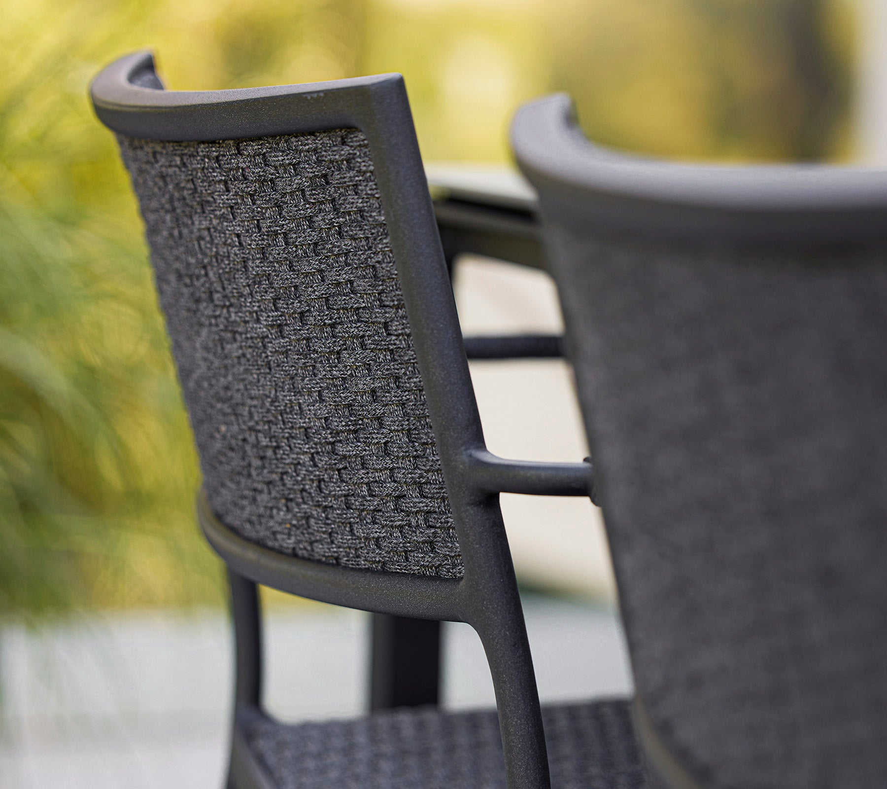 Närbild av en stilren stol med en vävd ryggstöd som visar en modern design i grå nyanser. Perfekt för samtida utrymmen.