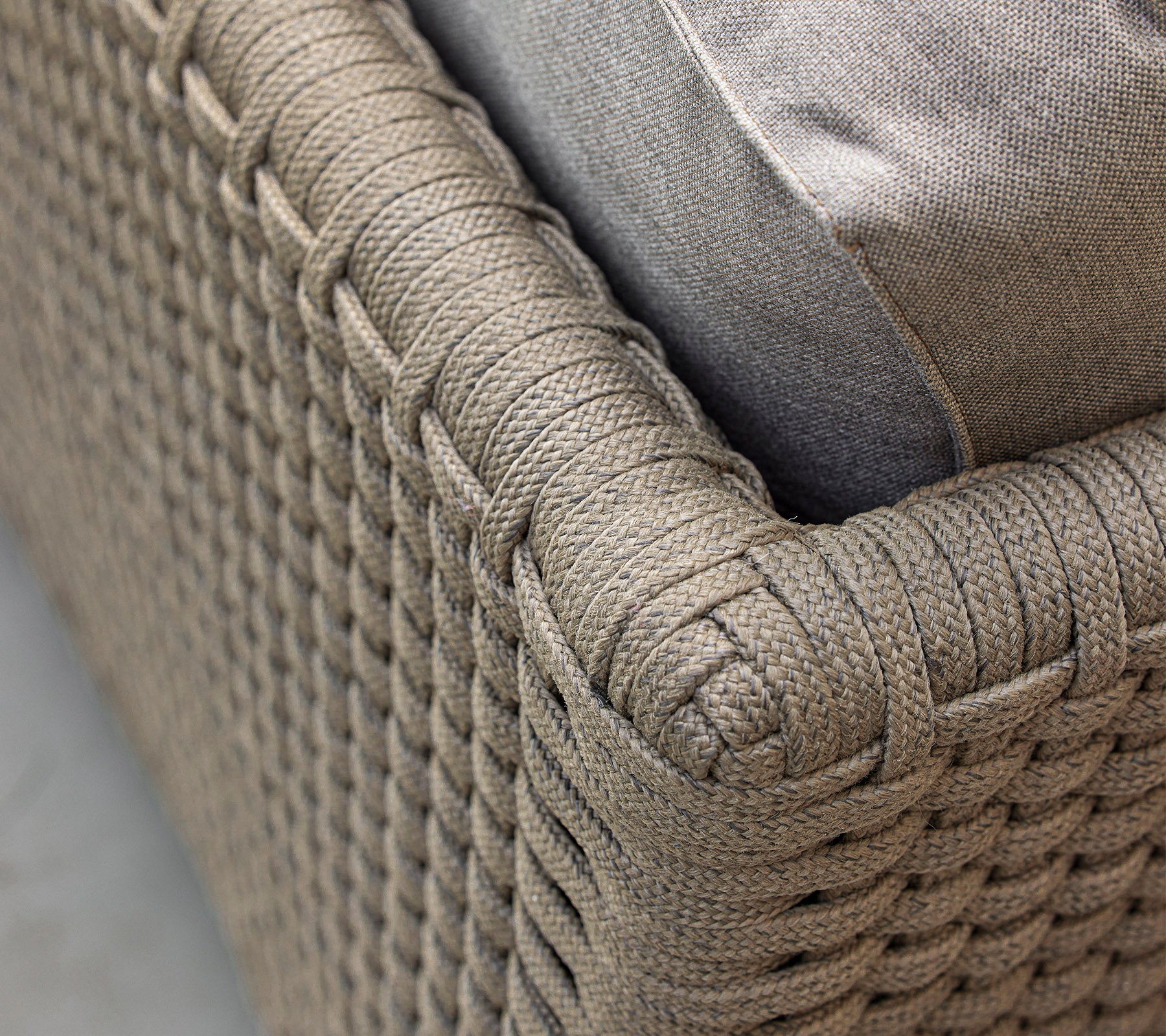 Närbild av en vävd, texturerad möbelbit med en mjuk kudde som framhäver dess intrikata design och neutrala färgschema.