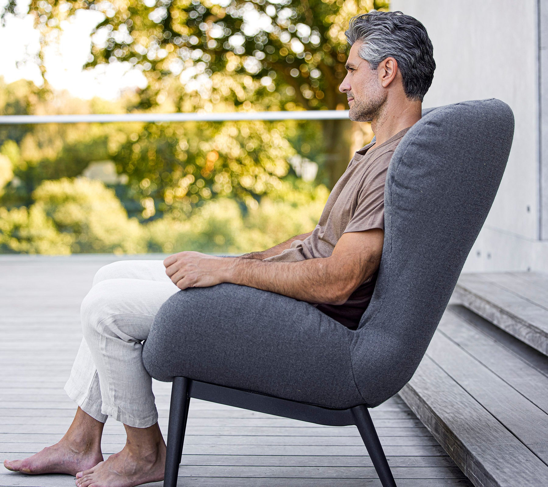 Man som sitter bekvämt i en modern stol med en slank design, som visar mjukt tyg och en elegant, minimalistisk form.