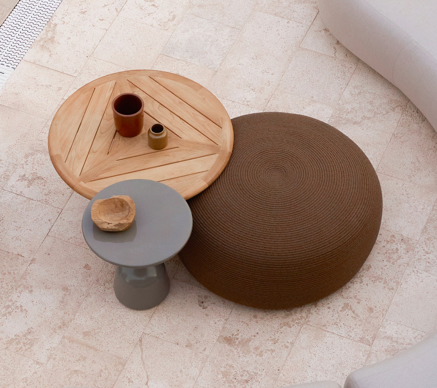 Ett stort runt fotpall i brunt bredvid ett träkaffebord med geometrisk design med små dekorativa föremål ovanpå.