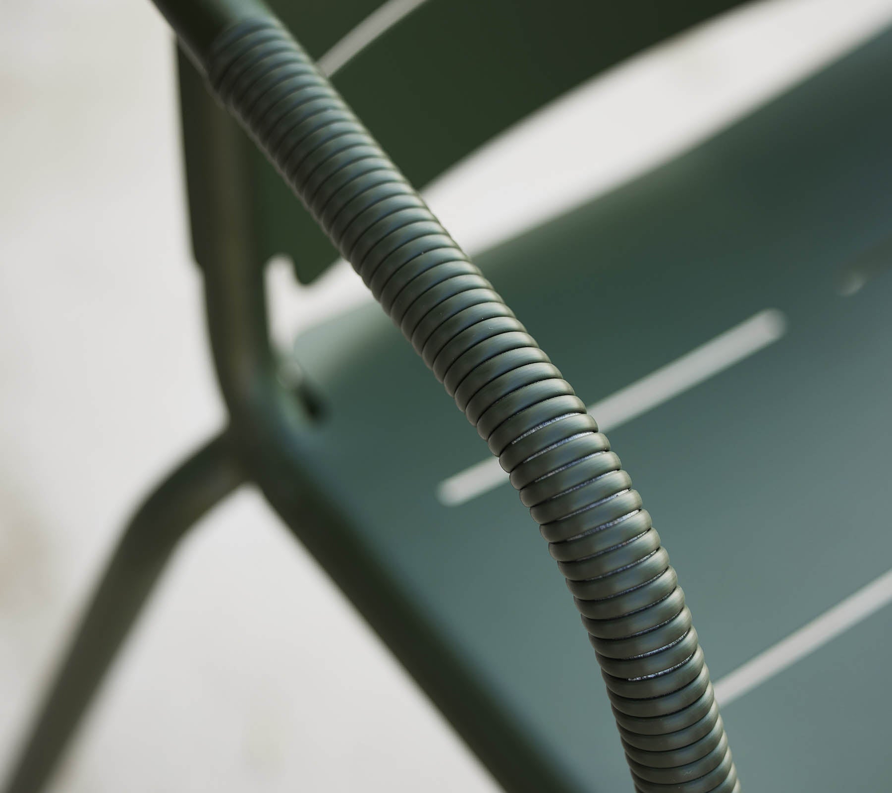 Närbild av en grön Copenhagen-stol, som framhäver dess böjda armstöd och eleganta design med subtila spalter på sätet.