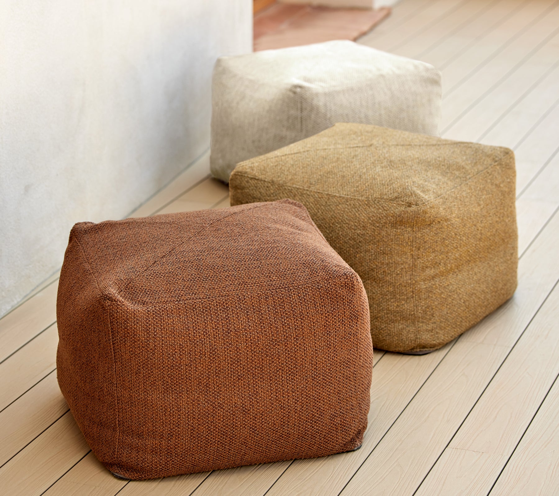 Tre strukturerade puffar i jordtoner av brunt, beige och tan, visade på en träytan. Idealiskt för mångsidig sittplatser och dekoration.