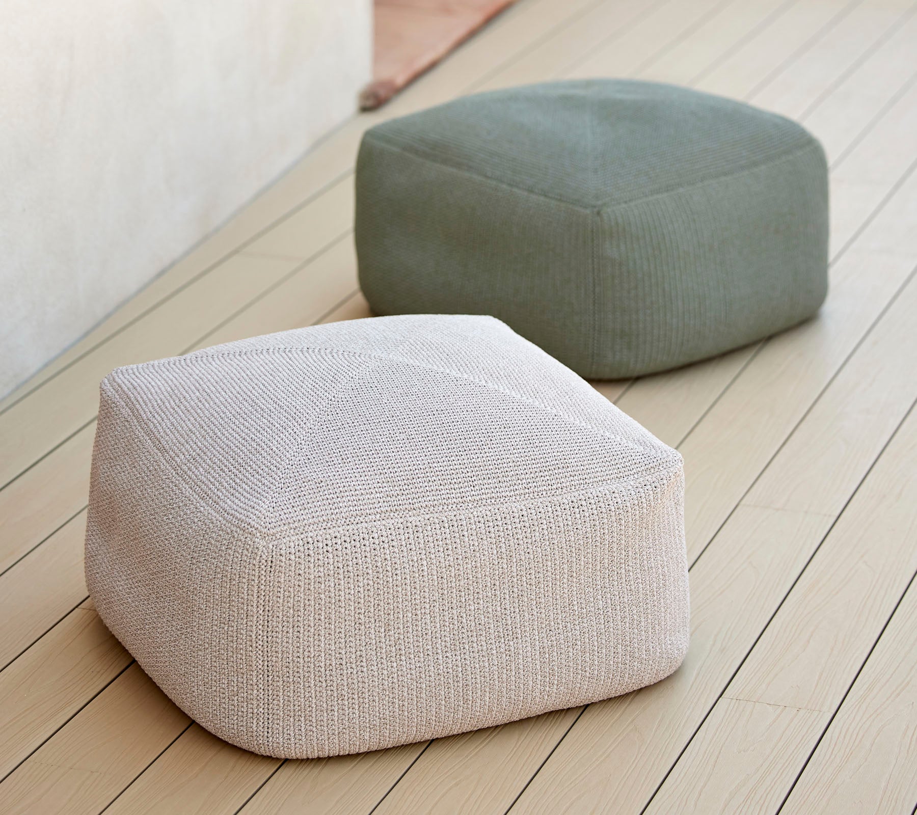 Två stiliga, strukturerade poufer i neutrala toner, en vit och en grön, arrangerade på en jämn yta, idealiska för mångsidig sittplats.