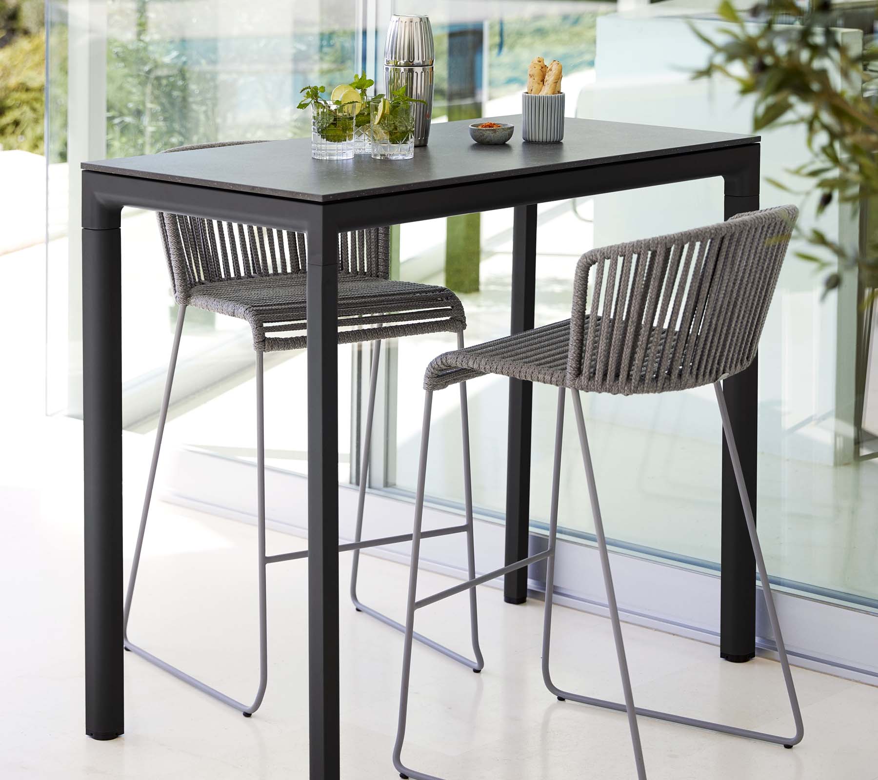 Modernt bord med två stiliga barstolar, präglat av en slimmad design, i kombination med dekorativa växter och minimalistiska mataccessoarer.