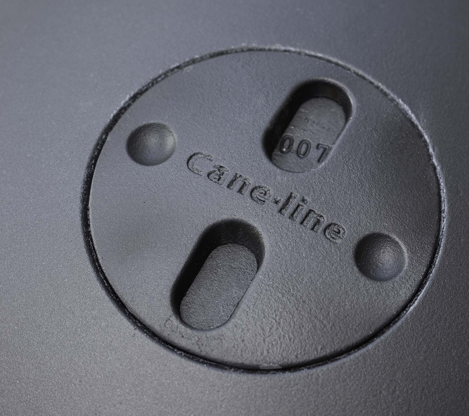 Närbild av ett cirkulärt inslag med ingraverad "Cane-line"-logotyp och två spår, en del av en eldstadsdesign.