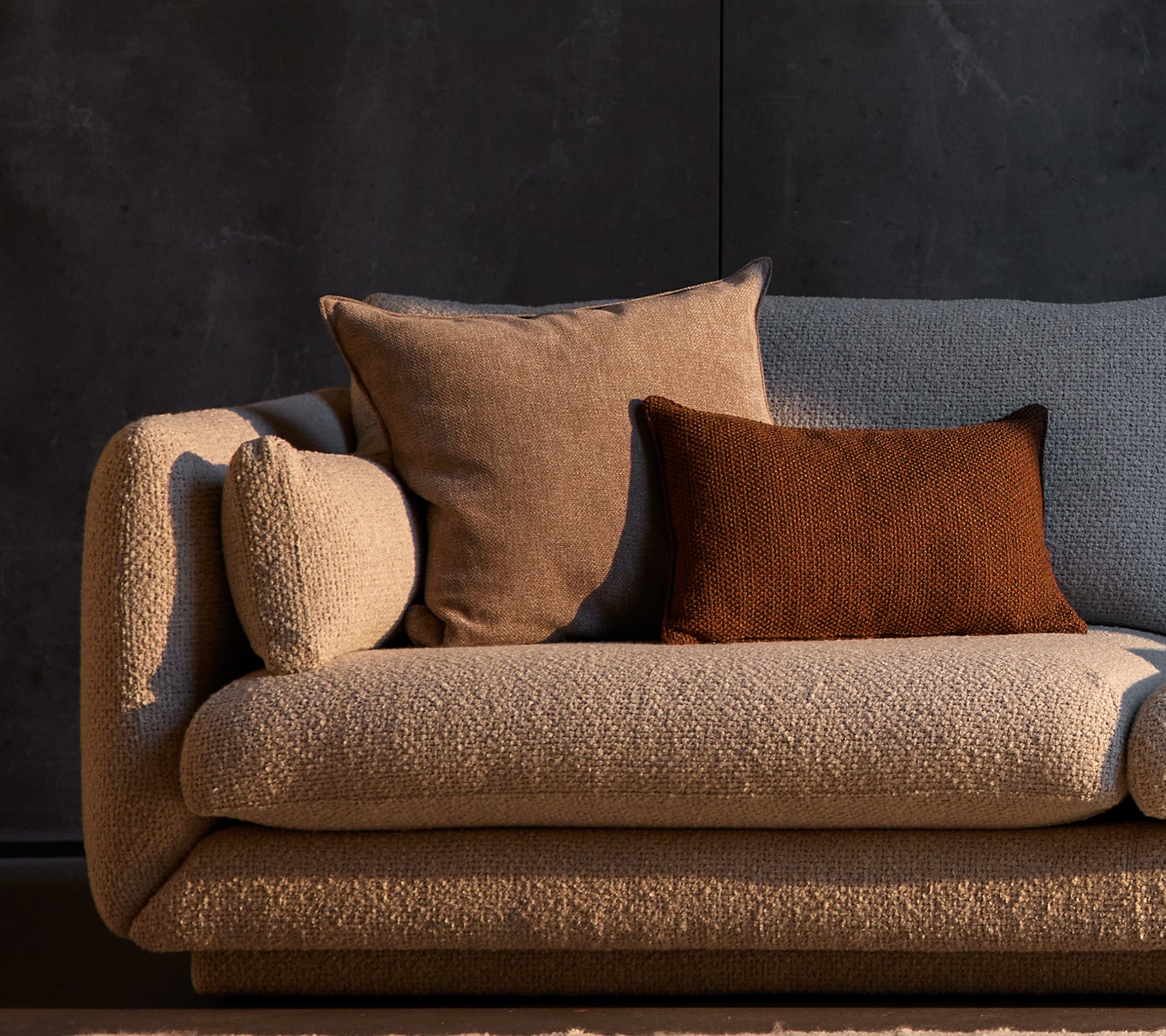Essence och Rise kuddar placerade på en strukturerad Bloom-soffa, med neutrala färger mot en mörk bakgrund.