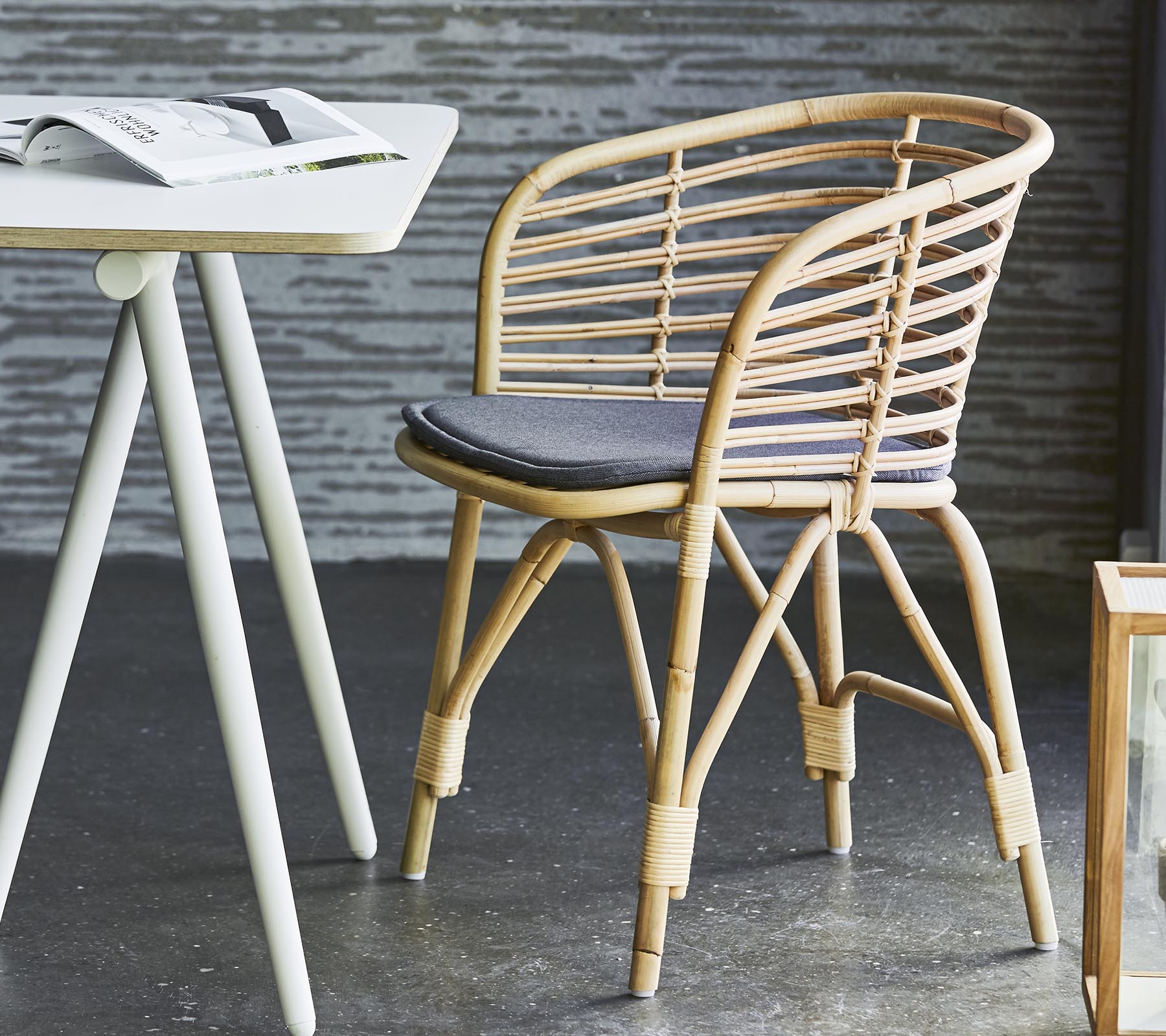 Stilfull korgstol med en grå kudde, tillsammans med ett enkelt bord och samtida inredning. Lämplig för avslappnad sittplats och avkoppling.