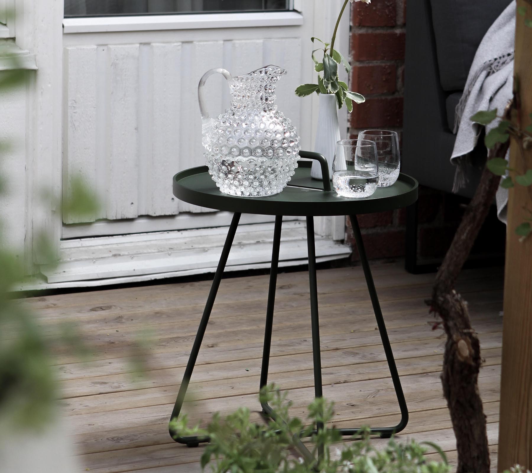 Ett stiligt grönt sidobord med en kristallkaraffel och två glas, kompletterat med frisk grönska i omgivningen.