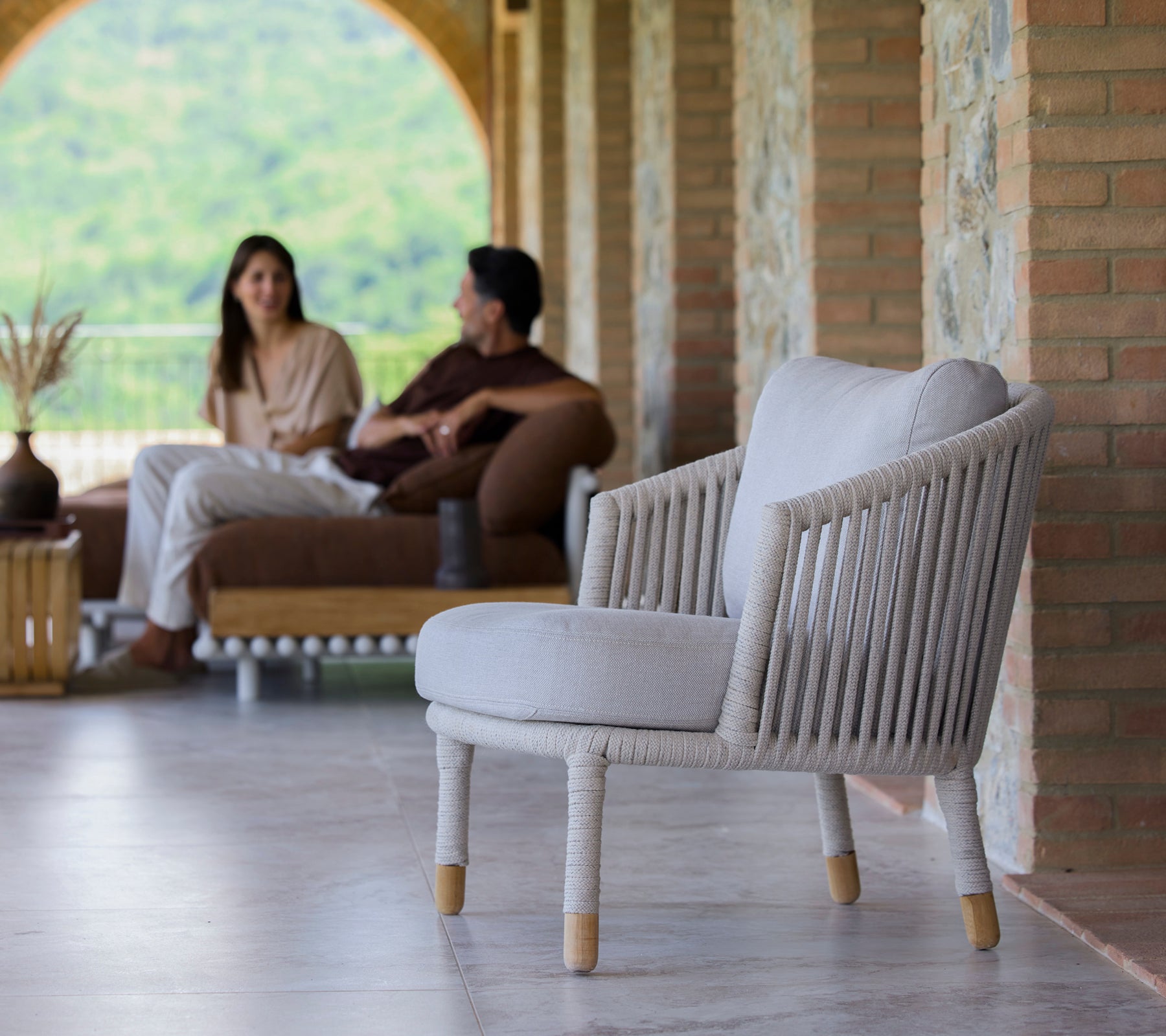 En sandfärgad loungestol med minimalistisk design, placerad i en lugn miljö med människor som är engagerade i samtal.