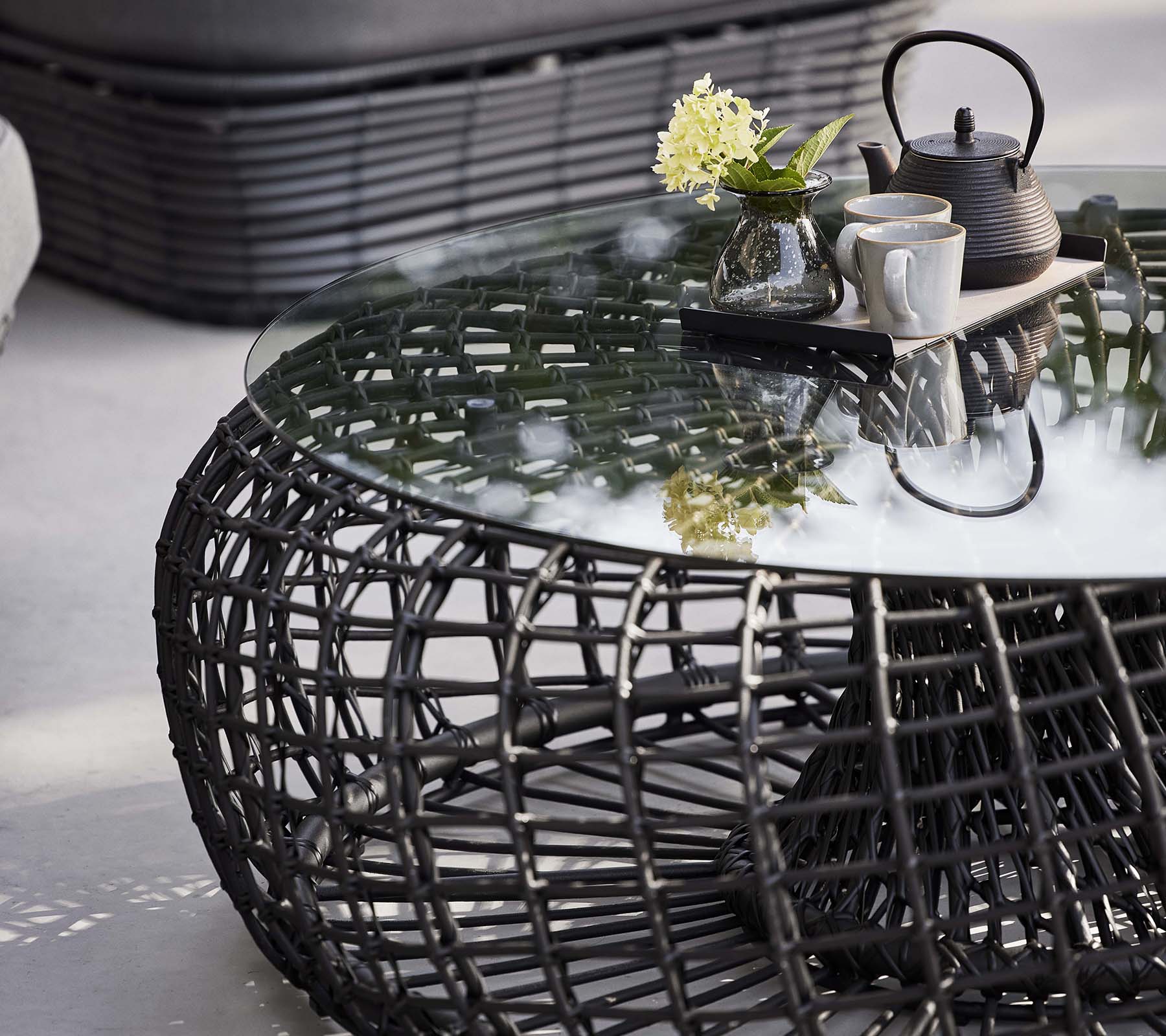 Nest soffbord med en vävd bas, en glasplatta och ett tekitt med blommor för en stilren, modern look.