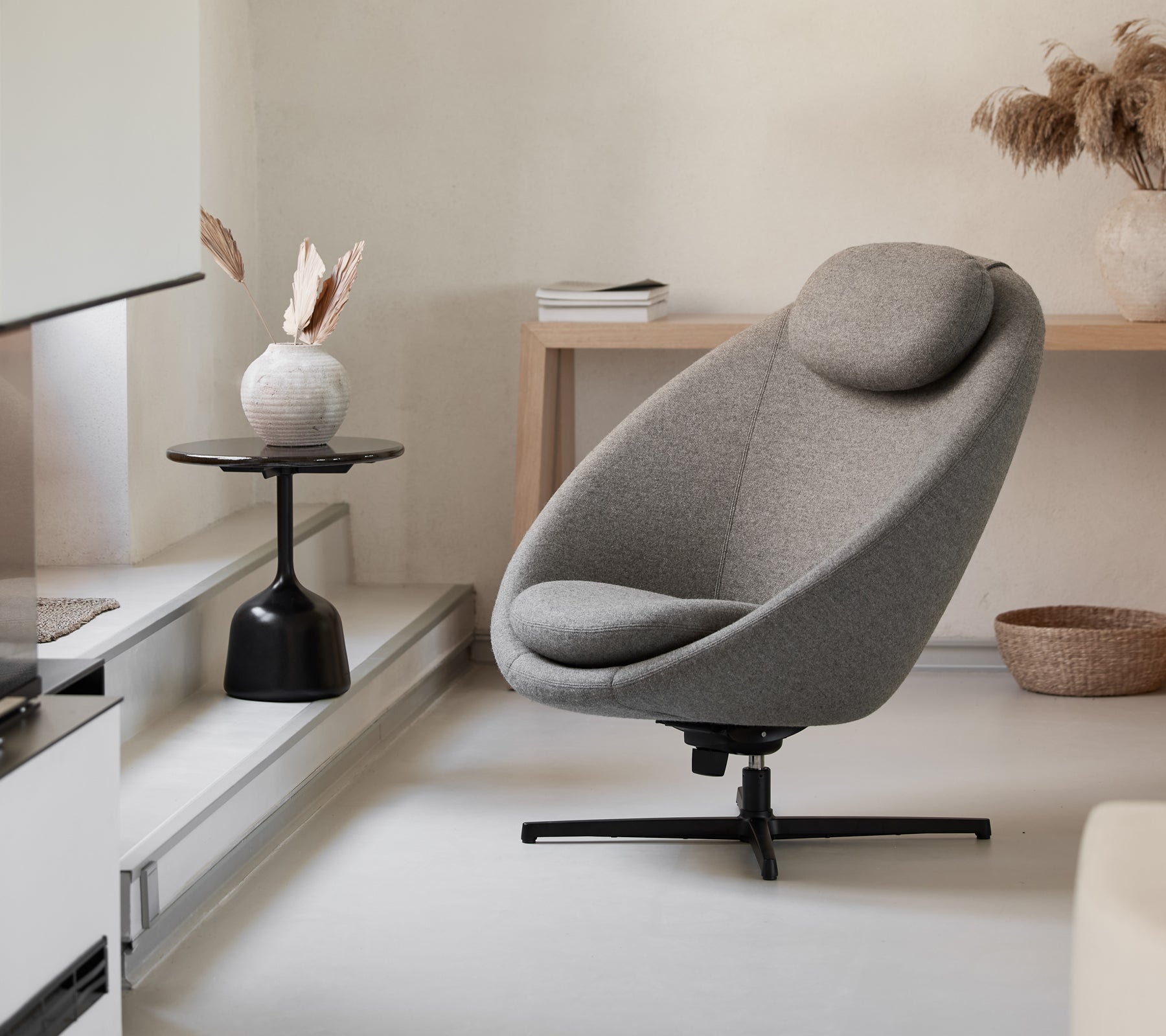 Stilfull grå stol med en böjd form och stödjande nackstöd, kompletterad med ett minimalistiskt sidobord och dekorativa element.