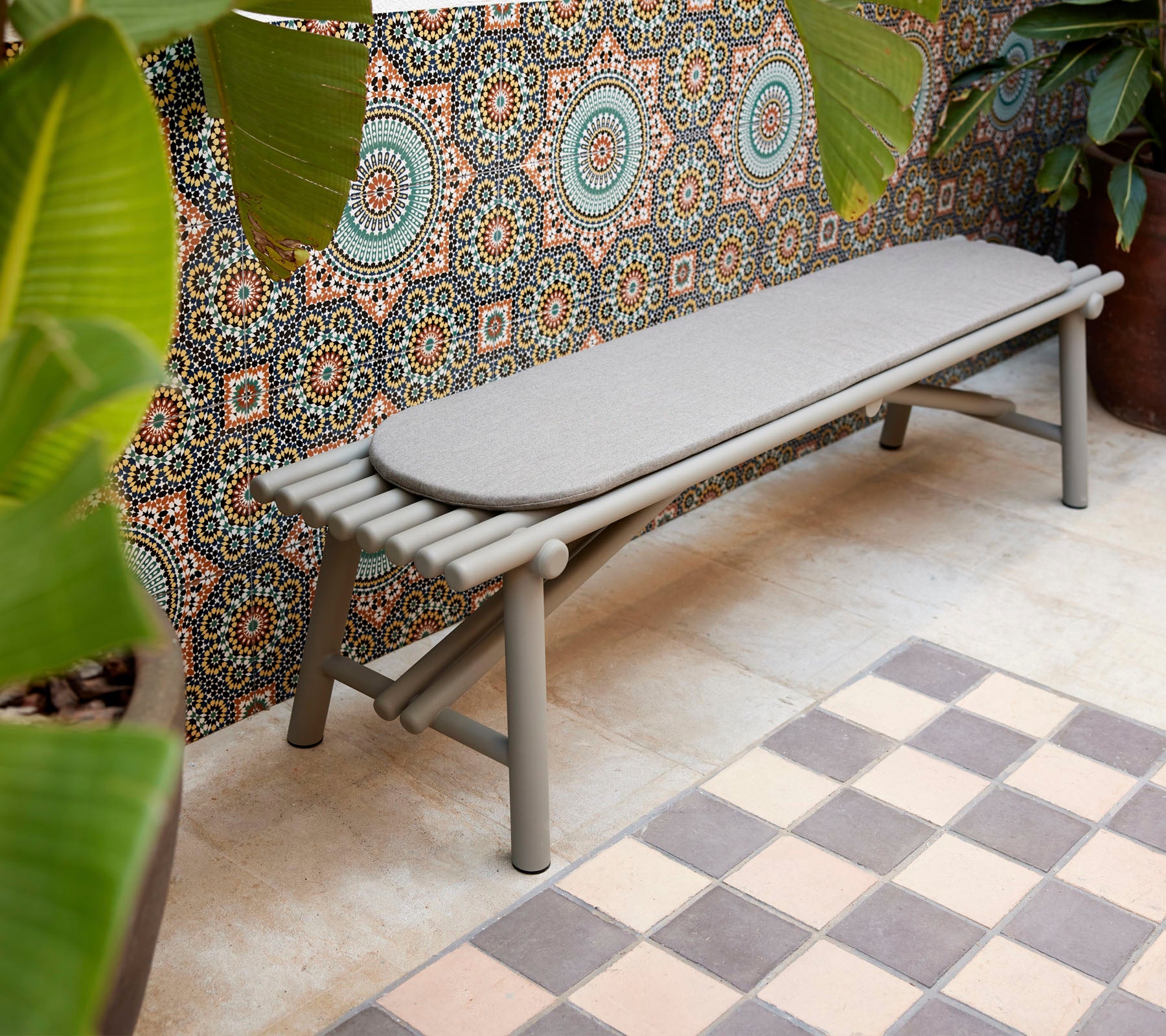 En slank bänk med stickliknande designelement, kompletterad med en geometrisk mönstrad bakgrund och livlig grönska.