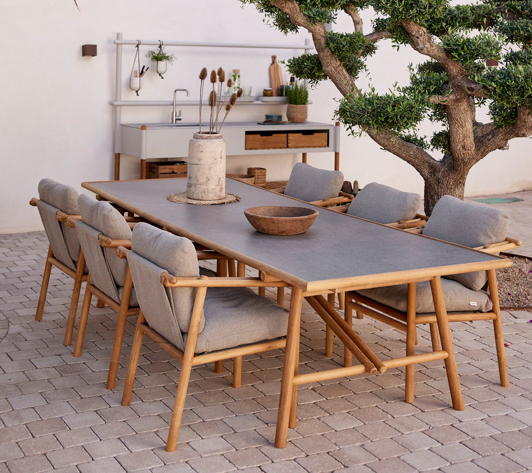 Teakmatbord omgärdat av bekväma stolar, med naturliga inslag och en minimalistisk inredningsstil.