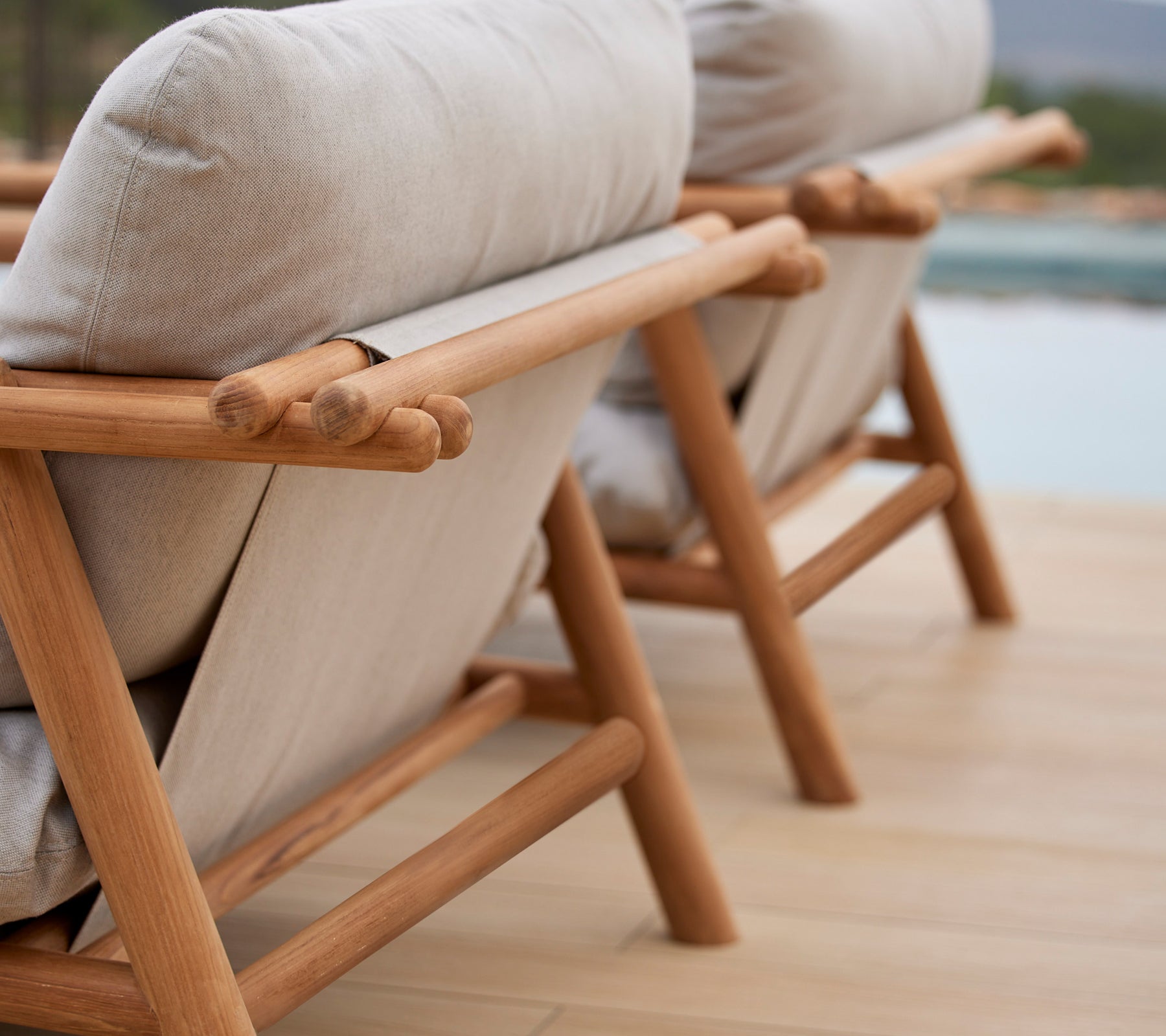 Två stiliga loungestolar med teakramar och bekväma beige kuddar, som visar en unik pinne-design på ryggstödet.