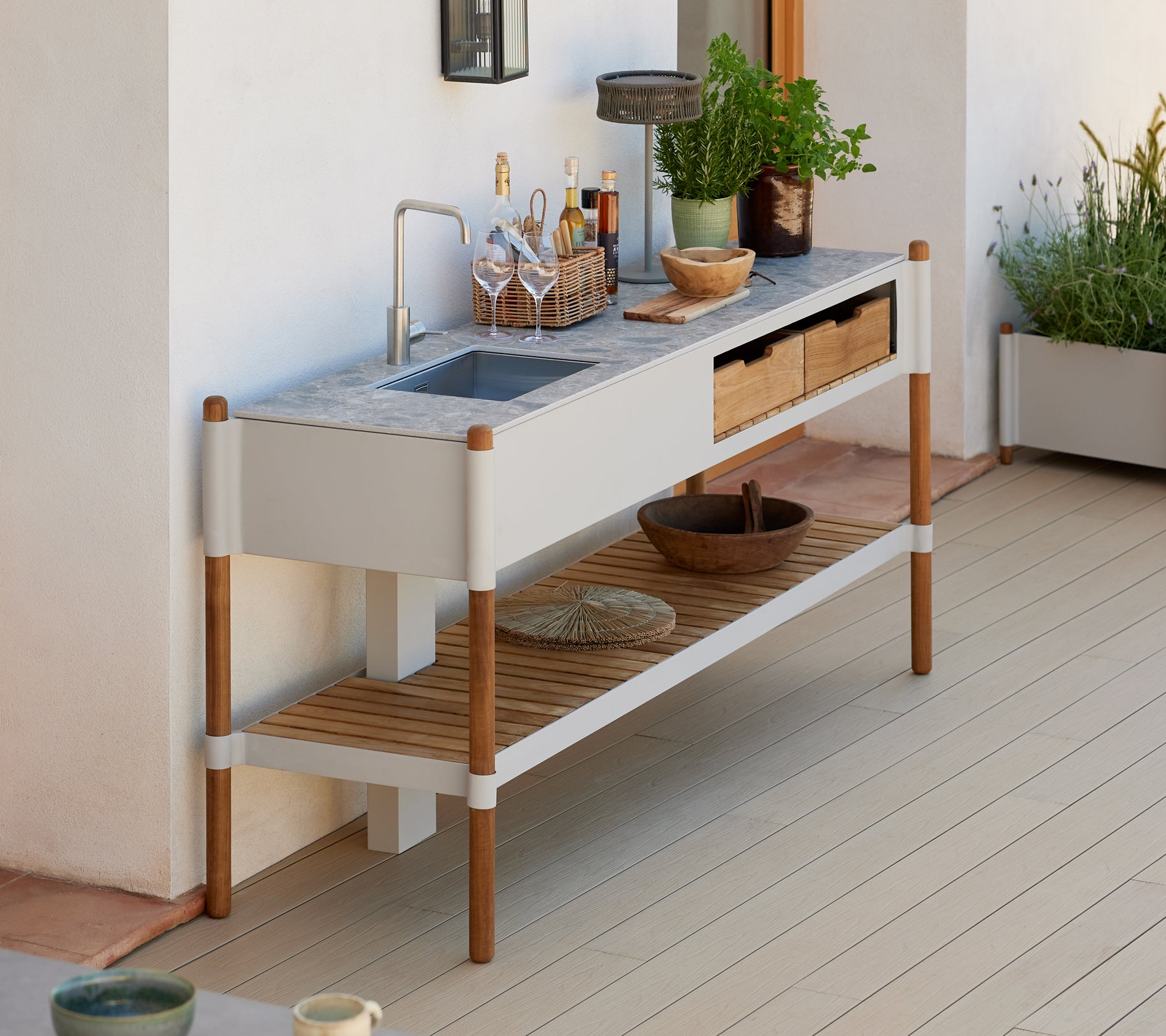 En modern, minimalistisk utomhusdisk med en bänkskiva i granit, träförvaringslådor och dekorativa växtarrangemang.