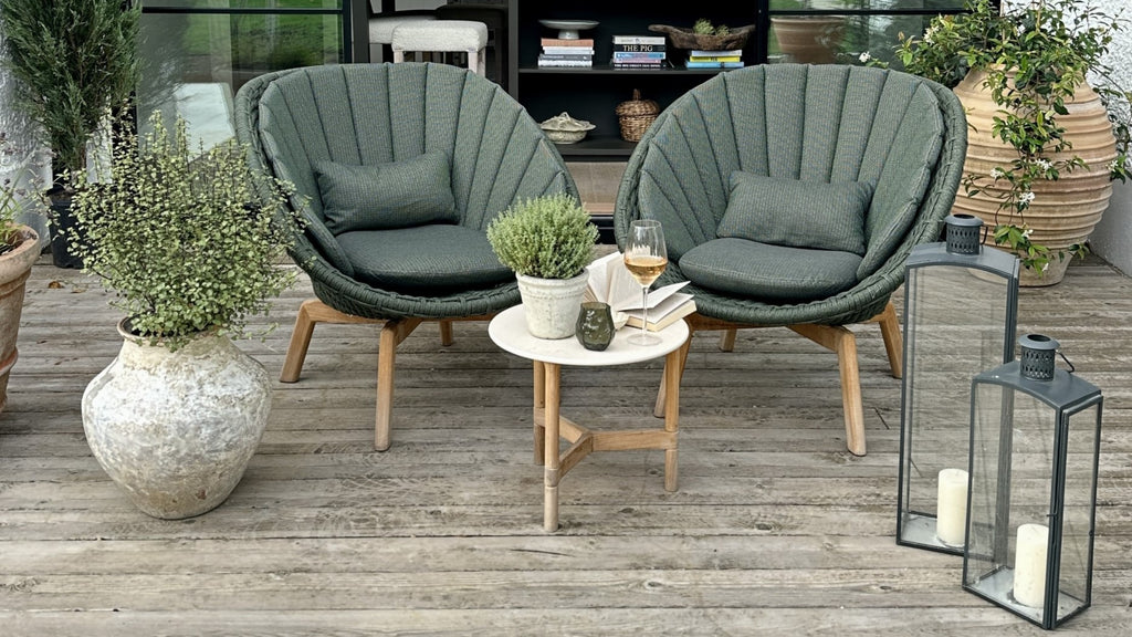 Two dark green lounge chairs with a small with side table in between on the veranda 