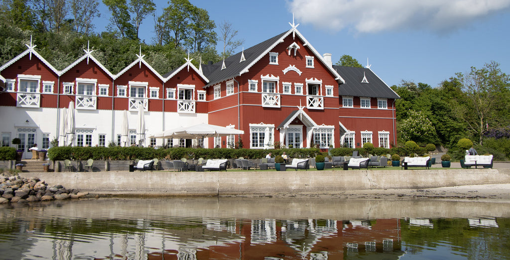 Dyvig Badehotel in Denmark, a characteristic red building with white exteriors. An outdoor lounge with many lounge sofas with sea view. 