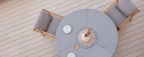 Rundt matbord med mjuka sittplatser, kompletterat med dekorativa tallrikar och en mittpunktarrangemang. Enkelt, elegant design.