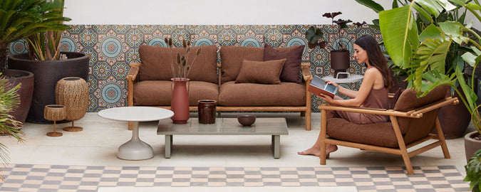 Ett mysigt sittområde med bruna fåtöljer, ett soffbord, växter och dekorativa väggplattor som skapar en avslappnad atmosfär.