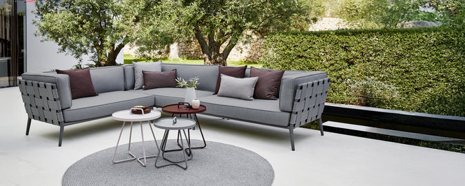 Modern grå sektion sofa med lila kuddar och ett runt kaffebord i ett loungeområde.