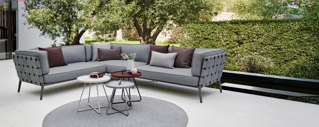 Modern grå sektion sofa med lila kuddar och ett runt kaffebord i ett loungeområde.