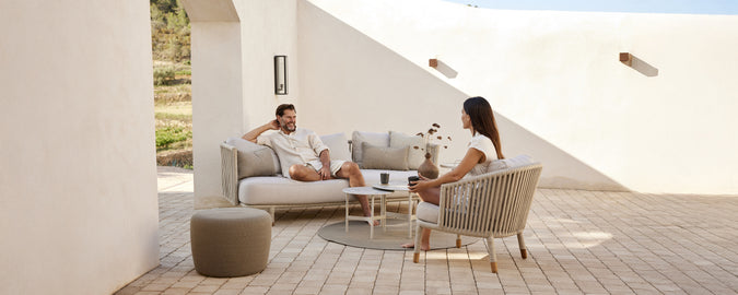 Modern loungeområde med beige soffa, vita kuddar, grå stol och runt bord.