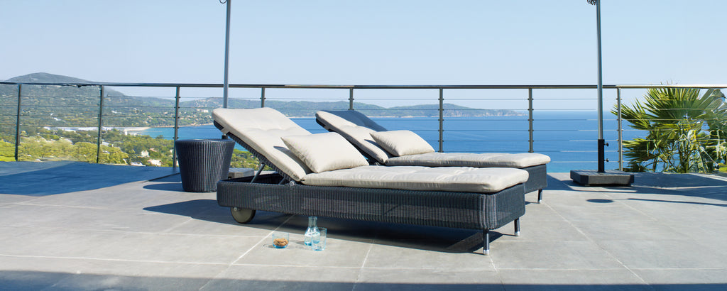 Två moderna grå och svarta fåtöljer på en terrass med utsikt över havet.