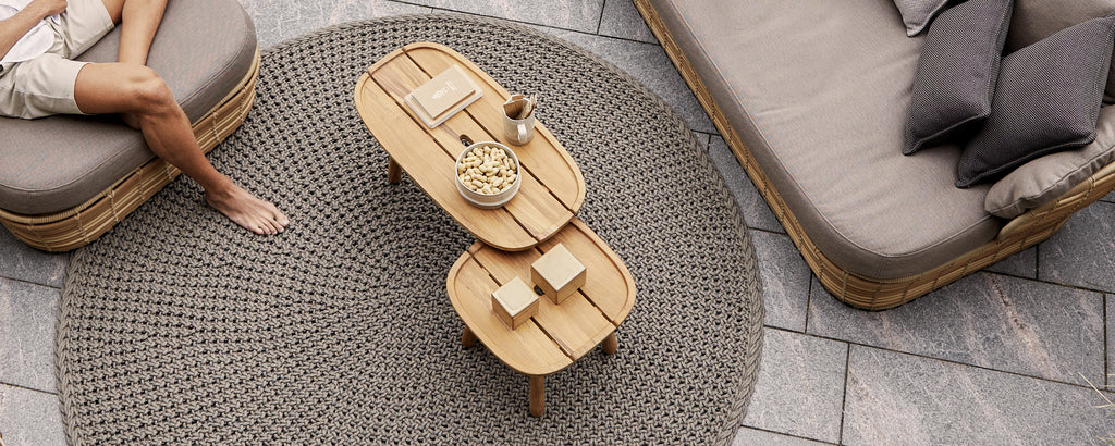 Modernt loungemiljö med ett brunt soffbord, en grå soffa och beige kuddar.