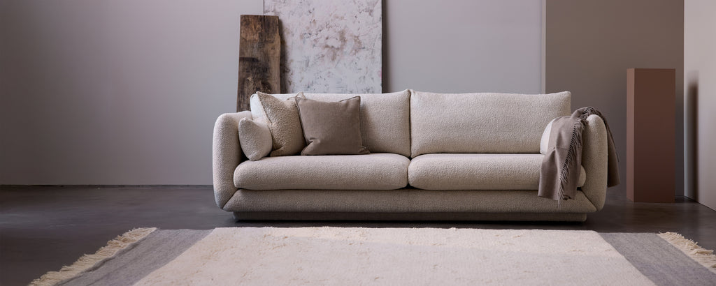 Beige soffa med grå kuddar i en modern loungemiljö.