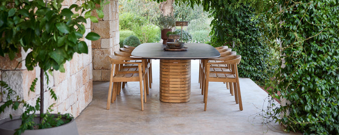 Utomhus trämatstolar kring ett svart bord i en grön trädgård.