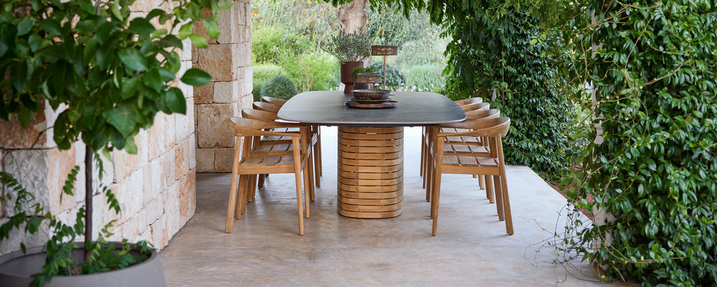 Utomhus trämatstolar kring ett svart bord i en grön trädgård.