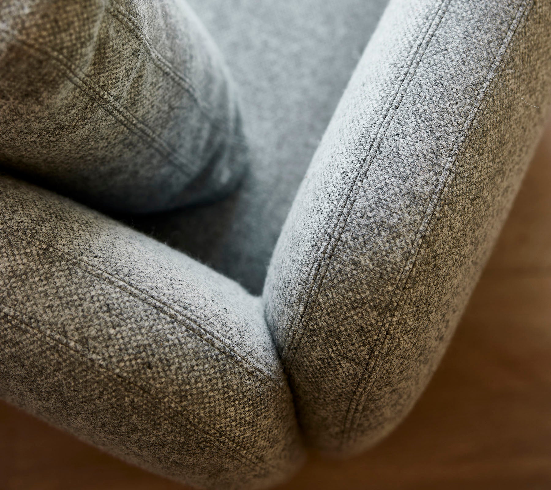 Närbild av en mjuk, texturerad grå klädd fåtölj som visar mjuka kurvor och detaljerad sömnad.