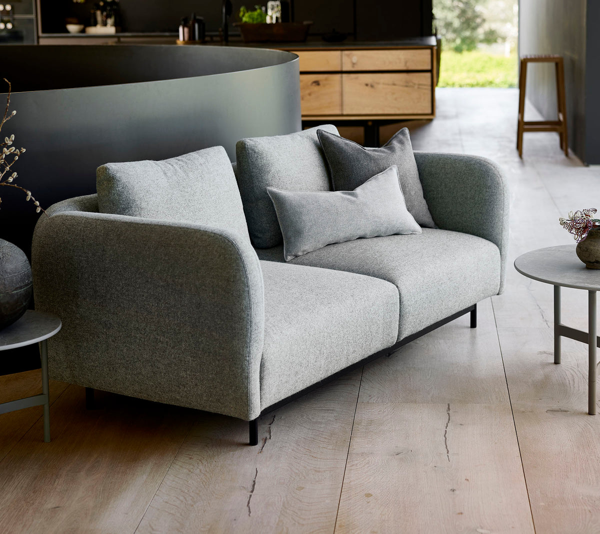 Modern grå soffa med mjuka kuddar, i par med ett litet runt bord, mot en minimalistisk bakgrund.