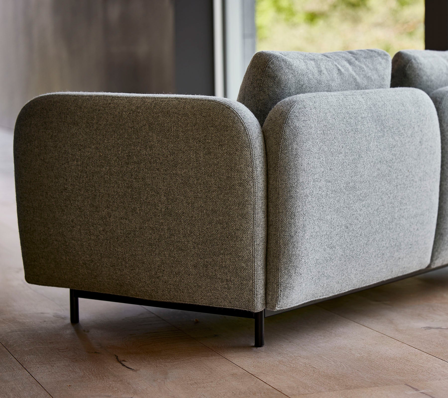 En modern grå klädd soffa med rundade kanter och eleganta svarta ben, som visar en minimalistisk design.
