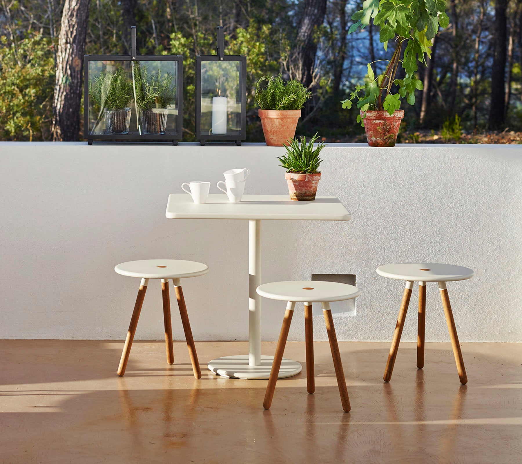 Ett minimalistiskt bord med tre matchande pallar, omgiven av krukväxter som skapar en lugn och inbjudande atmosfär.